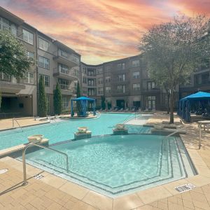 The Civic modern apartment building with large outdoor pool, blue cabanas, and lounge chairs under a partly cloudy sky.